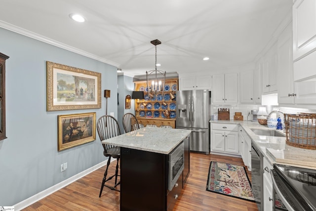 kitchen with sink, white cabinetry, hanging light fixtures, stainless steel appliances, and a kitchen island