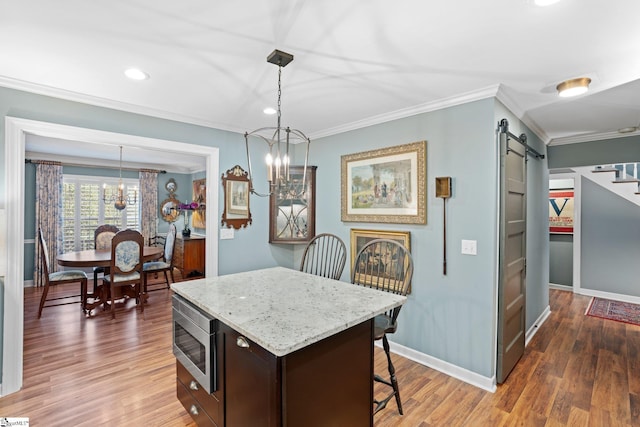 kitchen featuring a barn door, dark brown cabinets, stainless steel microwave, and decorative light fixtures