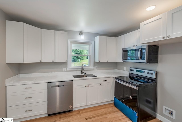 kitchen featuring appliances with stainless steel finishes, white cabinetry, sink, light stone countertops, and light wood-type flooring