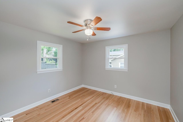 spare room featuring a ceiling fan, visible vents, baseboards, and wood finished floors