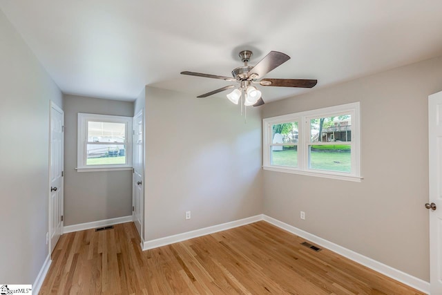 empty room with ceiling fan, a wealth of natural light, and light wood-type flooring