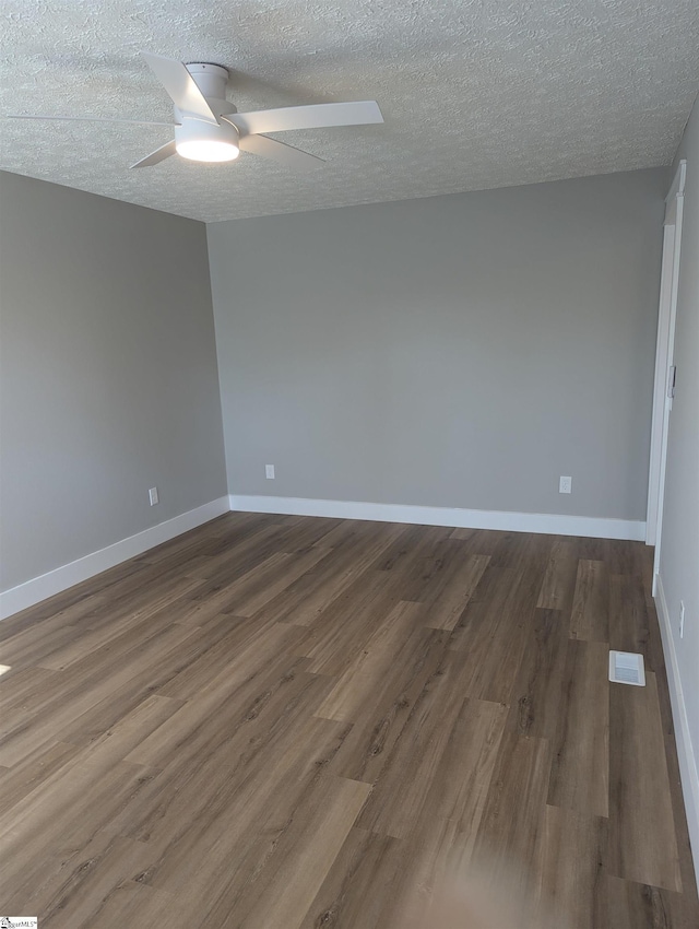 empty room with a textured ceiling, dark wood finished floors, a ceiling fan, and baseboards