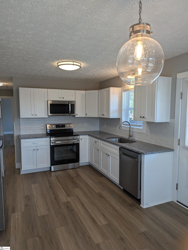 kitchen with stainless steel appliances, white cabinets, a sink, and decorative light fixtures