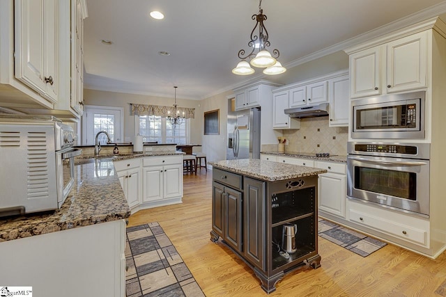 kitchen with pendant lighting, sink, stainless steel appliances, a kitchen island, and kitchen peninsula