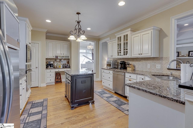 kitchen with appliances with stainless steel finishes, a kitchen island, decorative light fixtures, white cabinetry, and sink