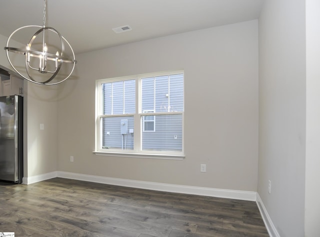 spare room featuring dark wood-type flooring and a chandelier