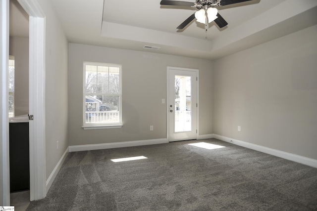 spare room featuring dark carpet, a tray ceiling, and plenty of natural light