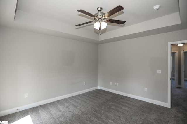 spare room featuring a raised ceiling, dark colored carpet, and ceiling fan