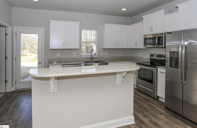 kitchen with light stone counters, stainless steel appliances, sink, and a kitchen island