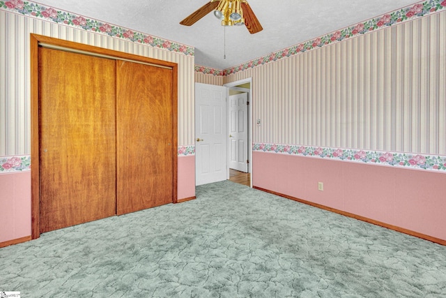 unfurnished bedroom featuring ceiling fan, a closet, a textured ceiling, and carpet flooring