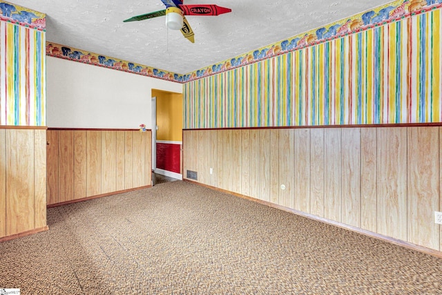 spare room featuring ceiling fan, wooden walls, a textured ceiling, and carpet flooring