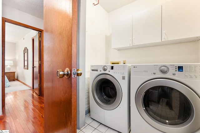 washroom featuring cabinets, separate washer and dryer, light hardwood / wood-style floors, and a textured ceiling