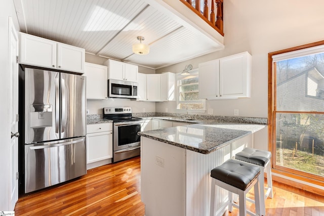 kitchen featuring stainless steel appliances, white cabinetry, a kitchen breakfast bar, and dark stone counters