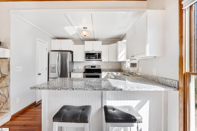 kitchen with appliances with stainless steel finishes, white cabinetry, a kitchen breakfast bar, kitchen peninsula, and light stone countertops