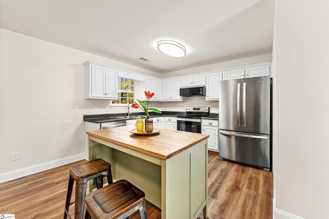 kitchen with a breakfast bar, appliances with stainless steel finishes, butcher block counters, white cabinets, and light wood-type flooring