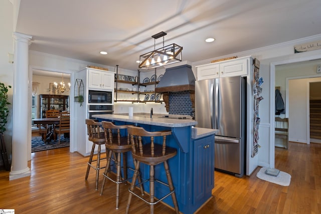 kitchen featuring a center island with sink, ornamental molding, black appliances, custom range hood, and white cabinets