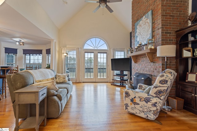 living room featuring french doors, high vaulted ceiling, a brick fireplace, ceiling fan, and light hardwood / wood-style floors