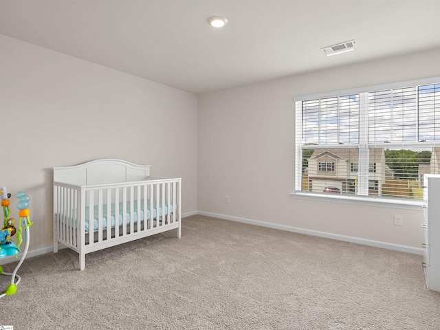 unfurnished bedroom with a crib, baseboards, visible vents, and carpet flooring