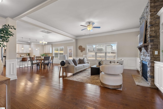 living room featuring a stone fireplace, dark wood-type flooring, ornamental molding, and ceiling fan with notable chandelier