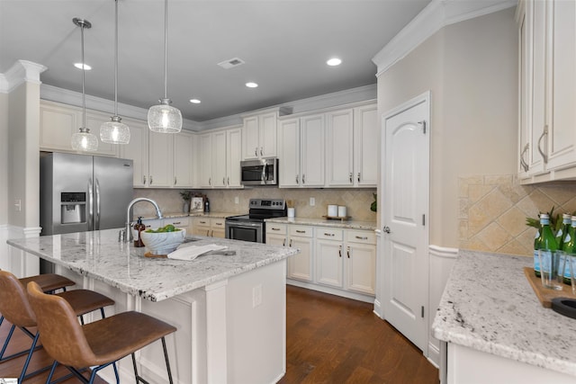 kitchen featuring appliances with stainless steel finishes, white cabinetry, a kitchen bar, hanging light fixtures, and a center island with sink