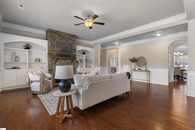 living room with built in shelves, ceiling fan with notable chandelier, dark wood-type flooring, and crown molding