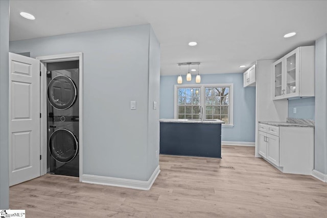 clothes washing area featuring stacked washer / drying machine, light hardwood / wood-style floors, and sink