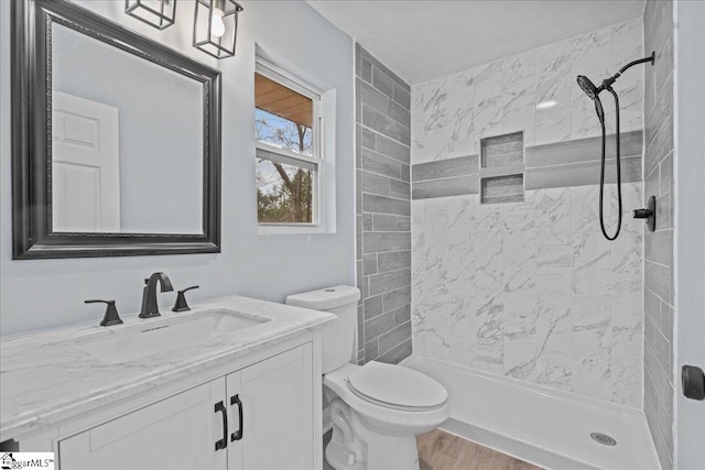 bathroom with hardwood / wood-style flooring, tiled shower, vanity, and toilet