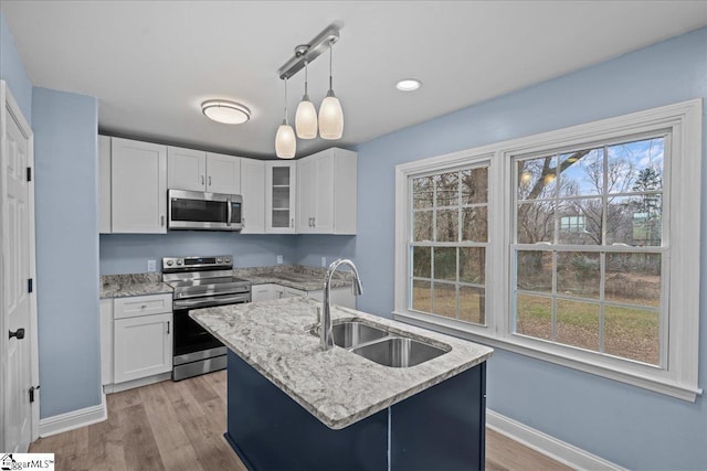 kitchen with sink, white cabinetry, light stone counters, appliances with stainless steel finishes, and an island with sink