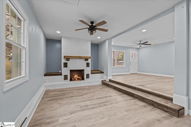 unfurnished living room with ceiling fan, a brick fireplace, and light hardwood / wood-style flooring