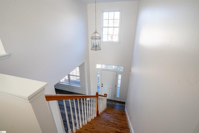 staircase with a notable chandelier, a towering ceiling, and wood-type flooring