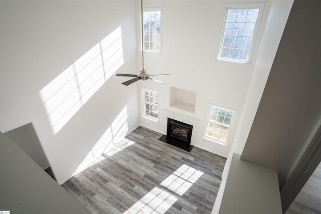 unfurnished living room featuring ceiling fan, wood-type flooring, and a high ceiling