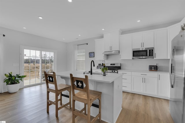 kitchen with sink, backsplash, stainless steel appliances, an island with sink, and white cabinets