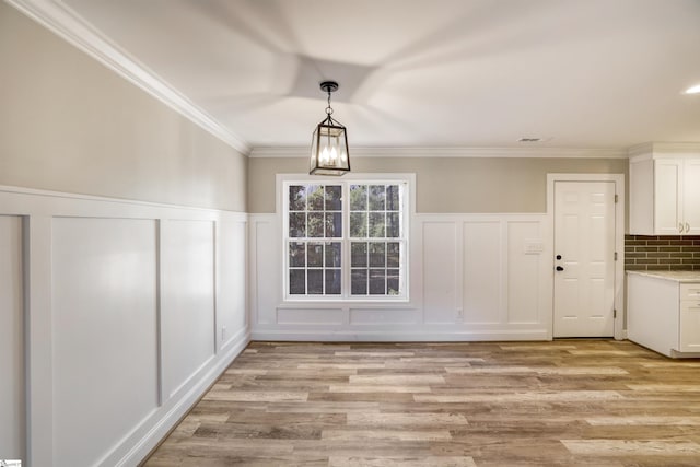 unfurnished dining area with ornamental molding, a chandelier, and light hardwood / wood-style flooring