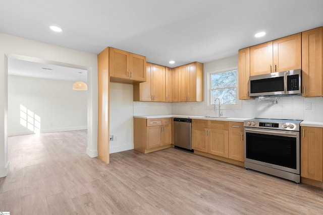 kitchen with appliances with stainless steel finishes, decorative light fixtures, sink, backsplash, and light hardwood / wood-style flooring