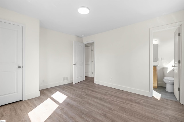 unfurnished bedroom featuring ensuite bath and light wood-type flooring