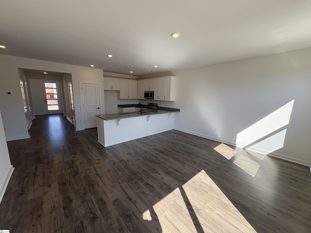 kitchen with white cabinetry, sink, a breakfast bar area, kitchen peninsula, and dark wood-type flooring