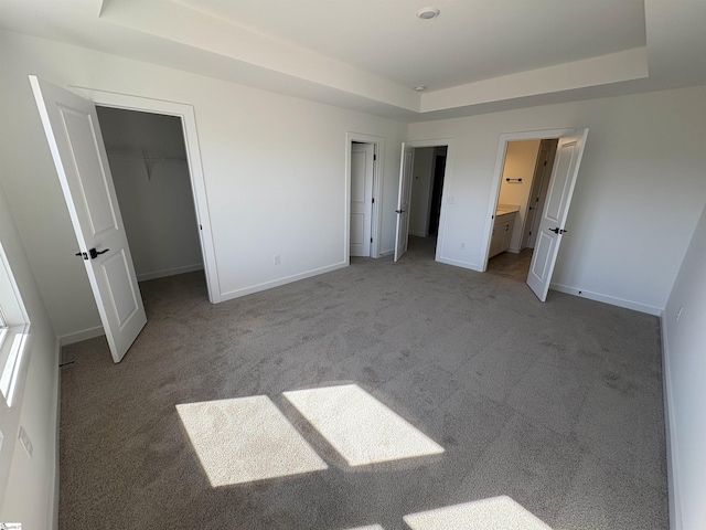 unfurnished bedroom featuring ensuite bathroom, a tray ceiling, light carpet, and a spacious closet