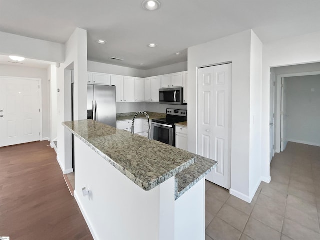 kitchen featuring sink, white cabinetry, stainless steel appliances, a center island, and dark stone counters