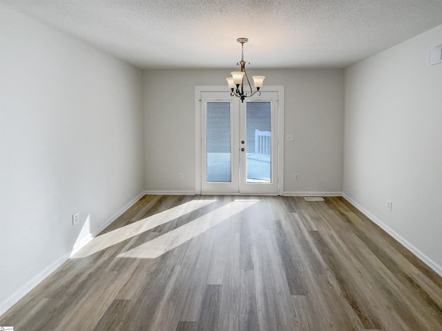 empty room with hardwood / wood-style flooring, a chandelier, french doors, and a textured ceiling