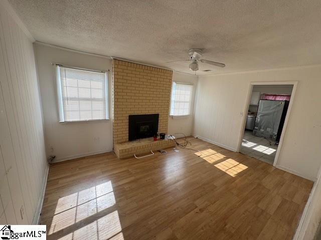 unfurnished living room with ceiling fan, hardwood / wood-style floors, ornamental molding, a textured ceiling, and a brick fireplace