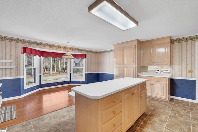 kitchen featuring hardwood / wood-style floors, light brown cabinetry, hanging light fixtures, a center island, and a textured ceiling