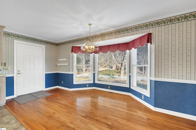 unfurnished dining area featuring wood-type flooring, ornamental molding, a notable chandelier, and a textured ceiling