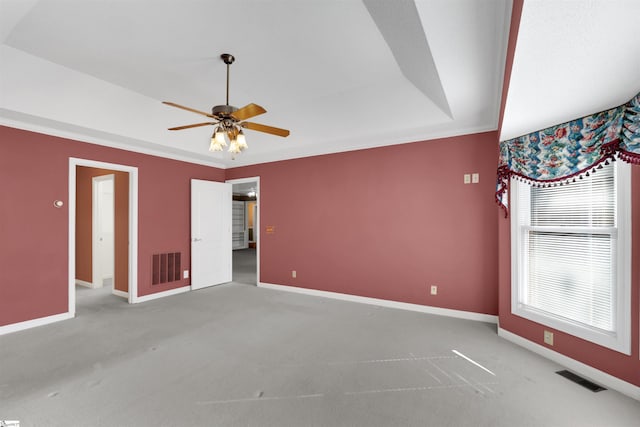 spare room with a raised ceiling, light colored carpet, and ceiling fan