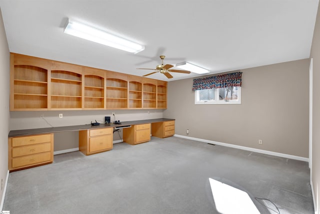 unfurnished office with light carpet, built in desk, and ceiling fan