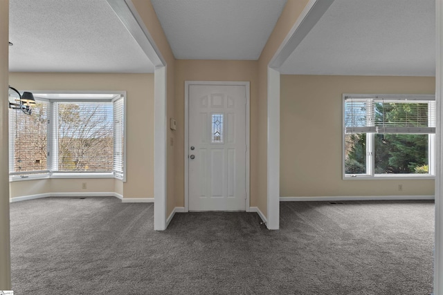 entryway with plenty of natural light, a chandelier, a textured ceiling, and dark colored carpet