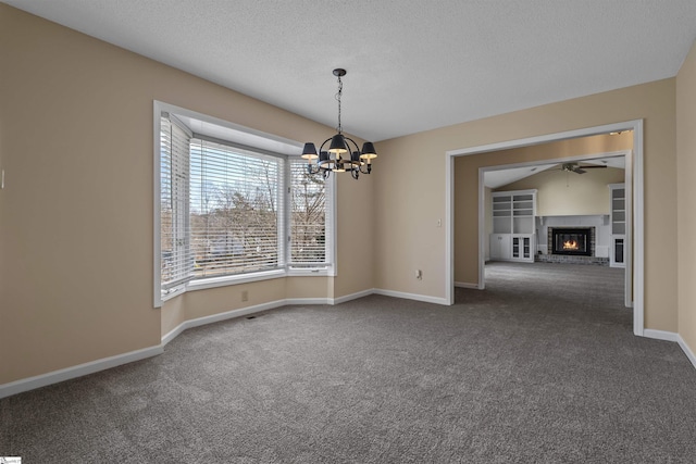 spare room with dark colored carpet, a brick fireplace, ceiling fan with notable chandelier, and a textured ceiling