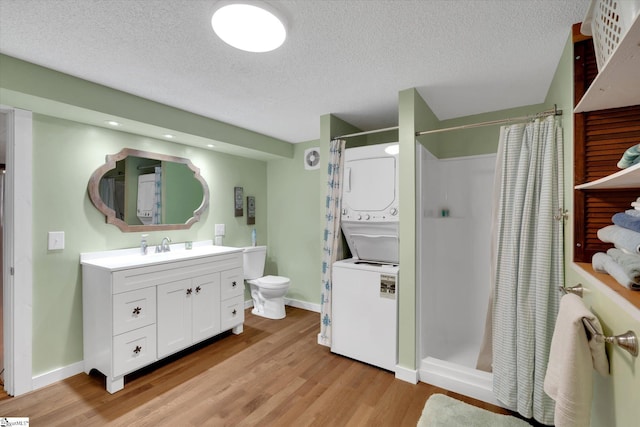 bathroom with stacked washer and dryer, a textured ceiling, vanity, curtained shower, and hardwood / wood-style floors