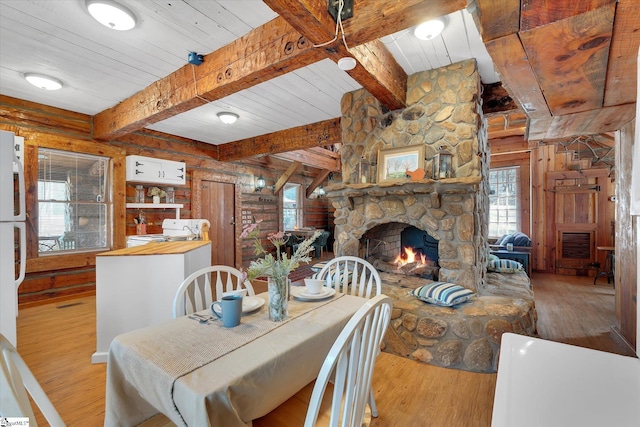 dining area featuring beamed ceiling, a stone fireplace, rustic walls, and light wood-type flooring