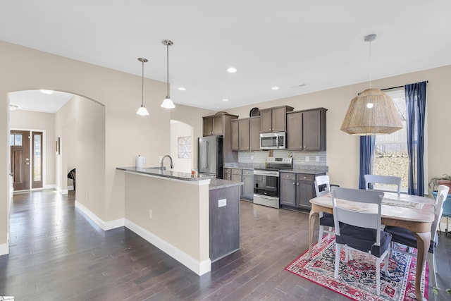 kitchen featuring dark wood-type flooring, appliances with stainless steel finishes, hanging light fixtures, backsplash, and kitchen peninsula