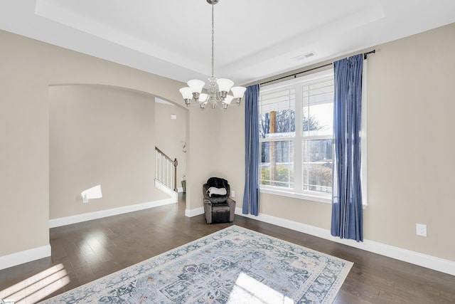 empty room with a raised ceiling, dark wood-type flooring, a wealth of natural light, and a notable chandelier